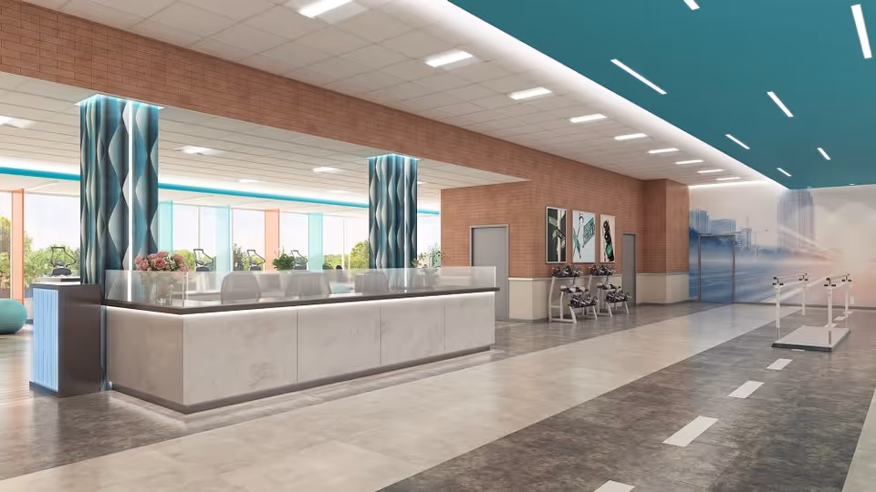 A modern, spacious interior of a senior living facility with a large reception desk in the foreground. The area features decorative columns with blue and white patterns, large windows letting in natural light, exercise equipment visible in the background, and a walking track with handrails on the right side. The walls have artwork and a mural depicting a cityscape.