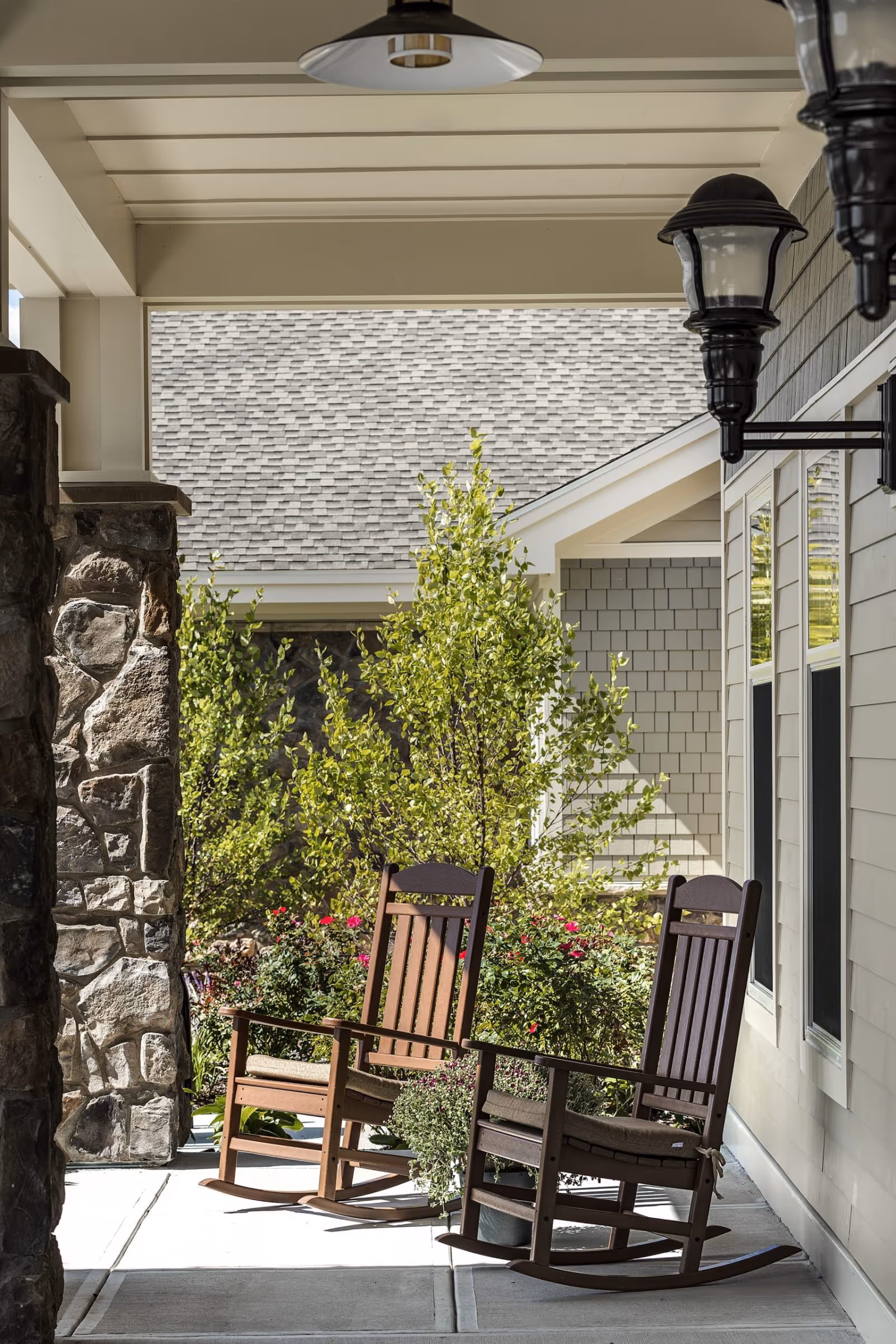 Covered front porch showing two wooden rocking chairs, potted plants, a stone column, and exterior lanterns.