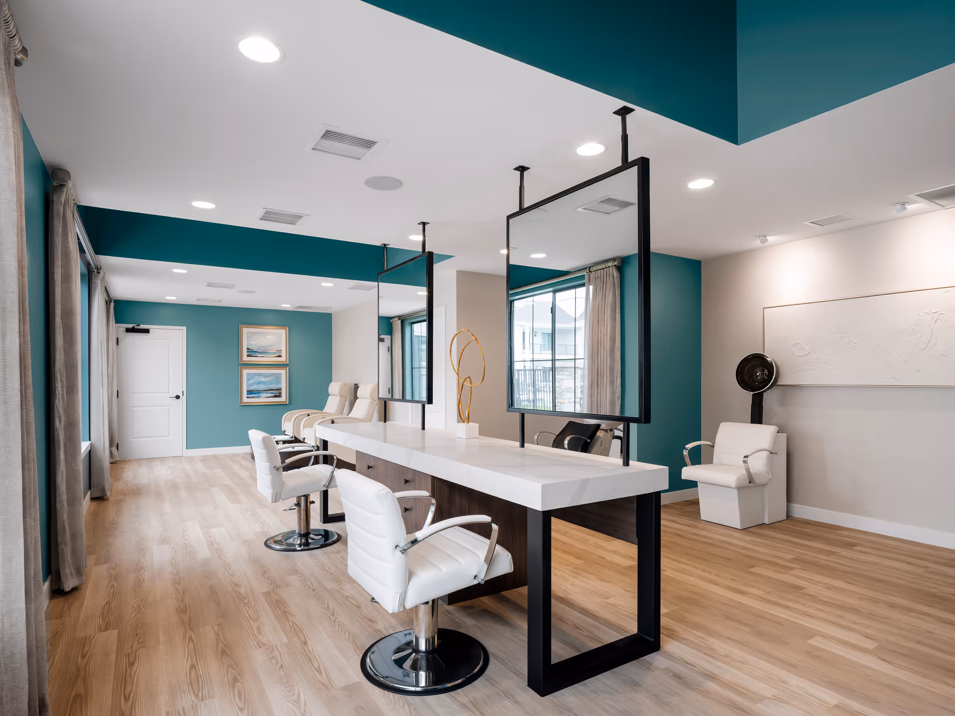 Bright salon-style interior with styling chairs, suspended mirrors, a long white counter and teal accent walls.