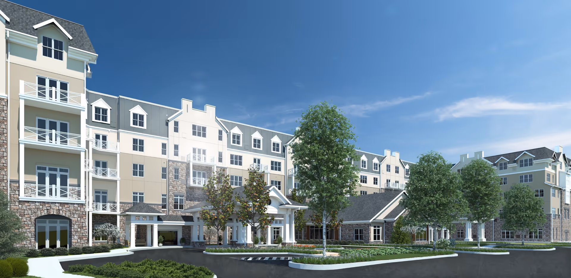 Exterior view of a multi-story senior living facility with beige and stone facade, multiple windows, balconies, and a covered entrance. The building is surrounded by landscaped greenery and trees under a clear blue sky.