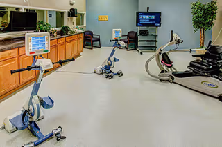 Indoor fitness room with stationary bikes, treadmills, a TV, and seating area in a senior facility.
