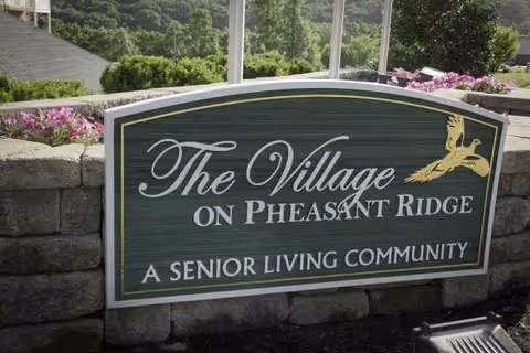 The Village on Pheasant Ridge senior living sign mounted on a stone wall with flowers.