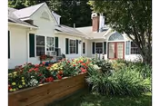 White single-story building with a raised flower bed of colorful flowers and a grassy lawn in front.