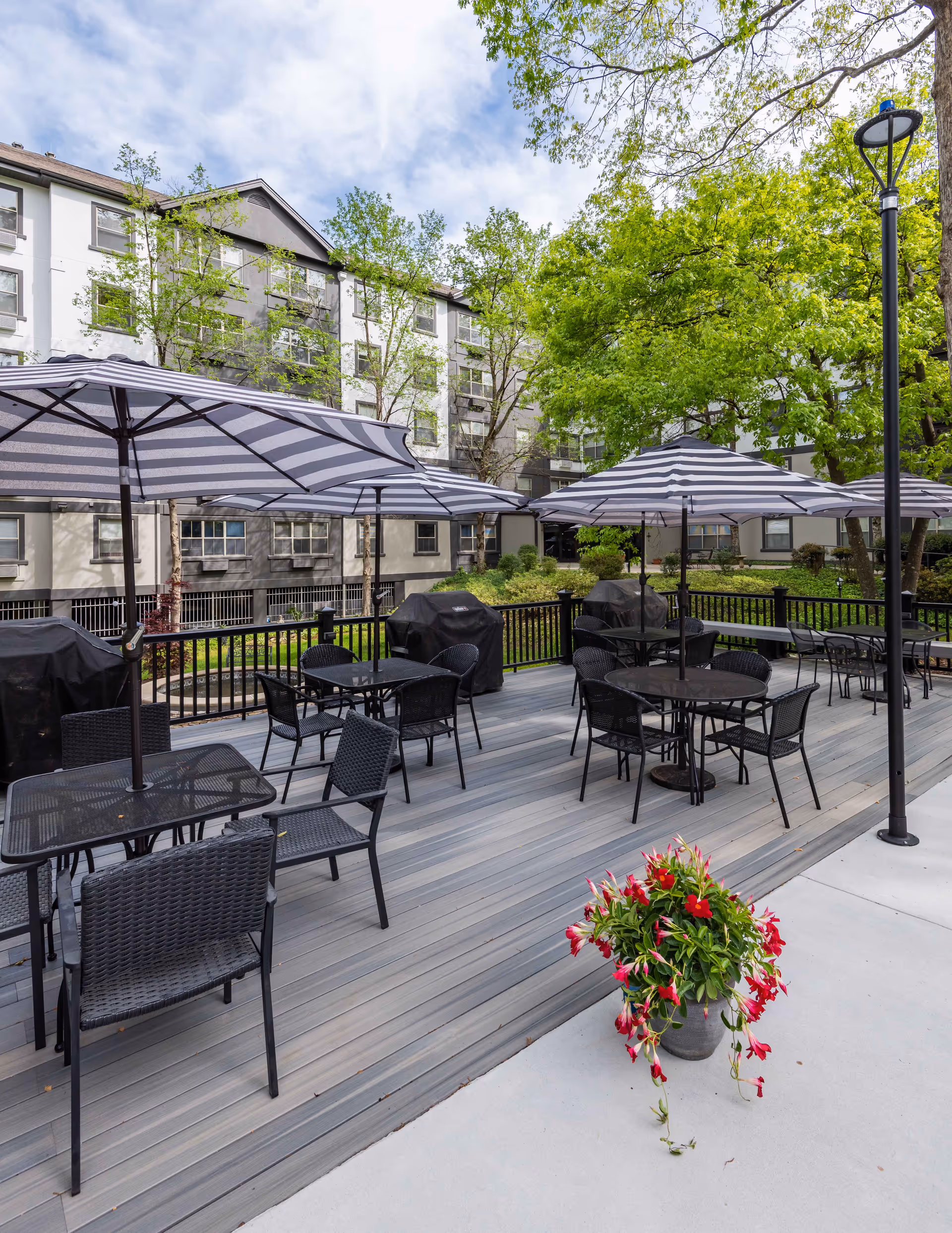Outdoor patio deck with striped umbrellas, tables and chairs in front of a multi-story residential building.