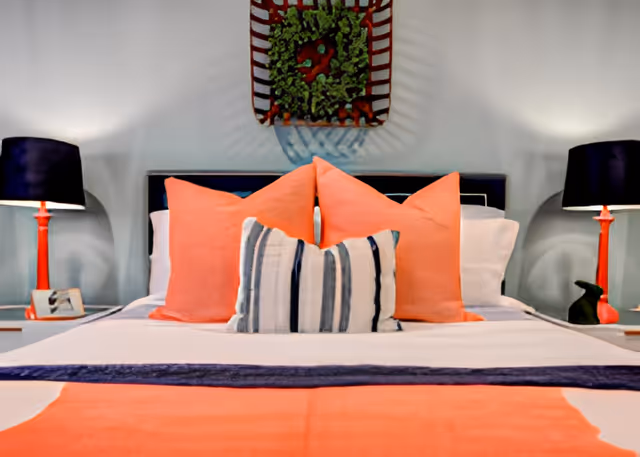 A neatly made bed with coral and striped pillows, bedside lamps, and wall decor above the headboard.