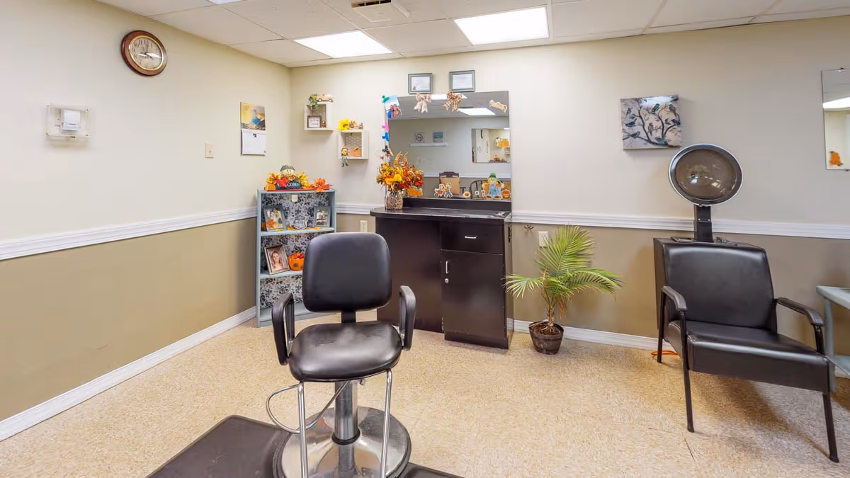 Small hair salon room with a styling chair, mirror, hooded dryer and seating.