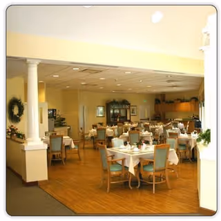 Bright dining room with multiple set tables and wooden chairs in a retirement community.