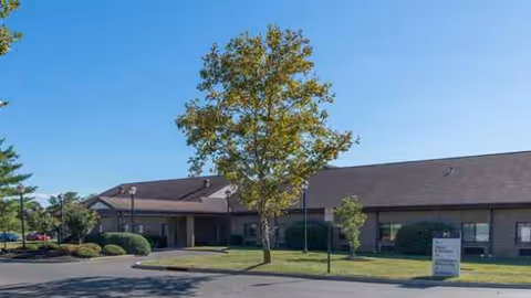 Exterior view of Atlas West Deptford senior living facility with trees, lawn, and parking.