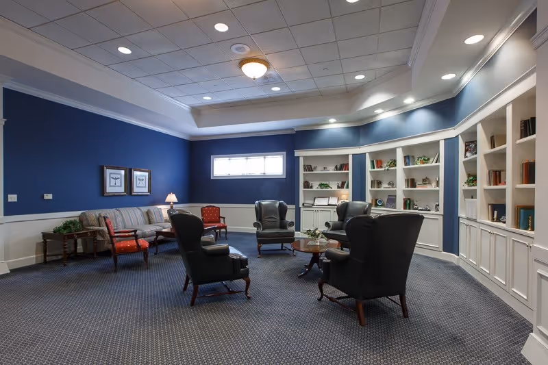 Comfortable common lounge with leather armchairs, a sofa, coffee tables and built-in bookshelves against blue walls.