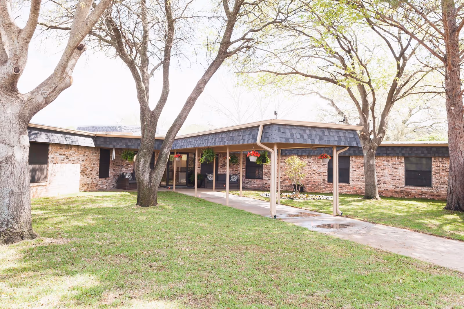 Front exterior of a one-story brick care center with a covered entrance walkway, lawn and trees.