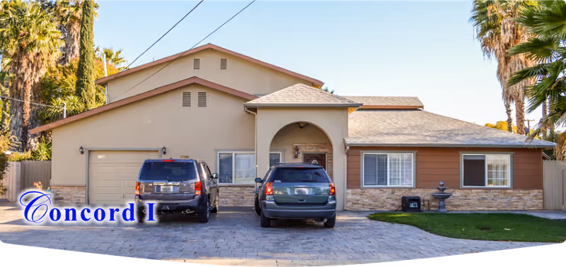 Front exterior of a single-story house with two SUVs parked in the driveway and palm trees in the background.