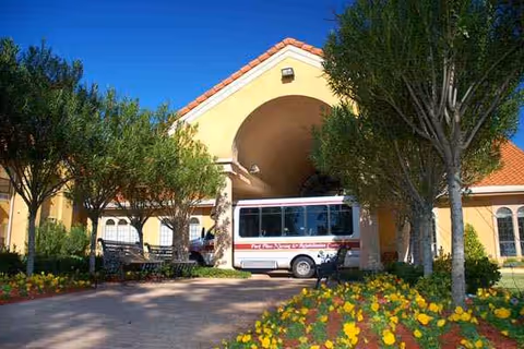 Yellow stucco nursing center entrance with a bus parked under a covered drop-off area.