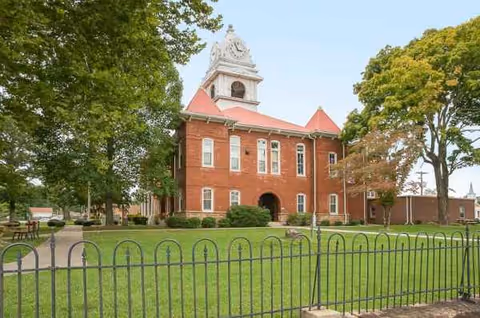 Front view of red brick Life Care Center with clock tower, manicured lawn, and fence.