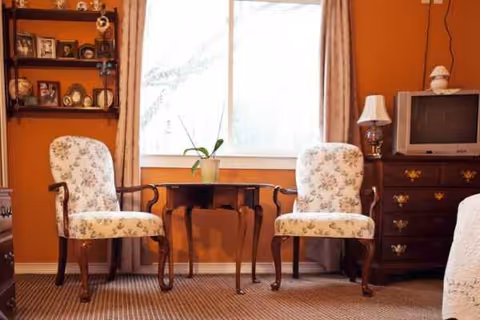 Two floral upholstered armchairs flank a small table with a plant by a window.