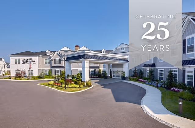 Exterior view of The Bristal Assisted Living at Mount Sinai building under a clear blue sky, showing the entrance with a covered driveway, landscaped greenery, and a sign on the building.