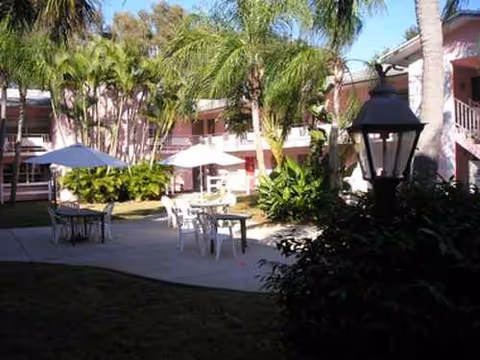 Outdoor courtyard with tables, umbrellas, and palm trees at Midway Manor ALF.
