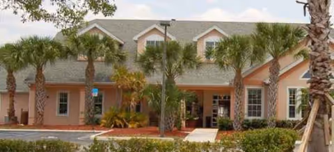 Peach-colored senior living building with palm trees and a covered entrance.