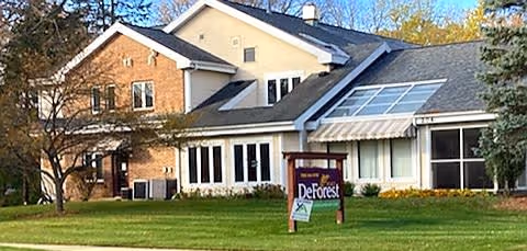 Front exterior of a two-story building with a lawn and a sign reading "DeForest".
