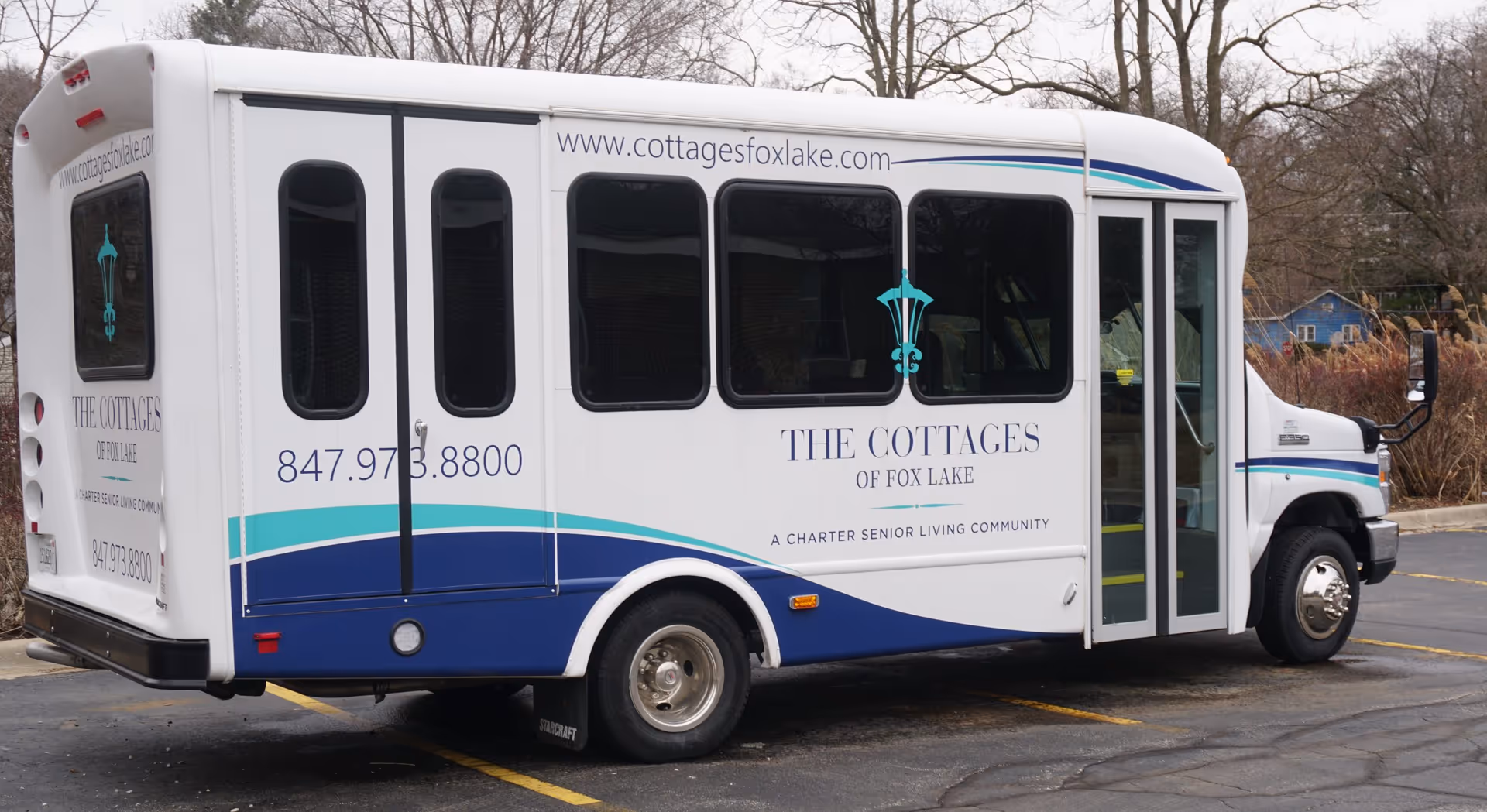 A white shuttle bus labeled "The Cottages of Fox Lake" with its website and phone number parked outdoors.