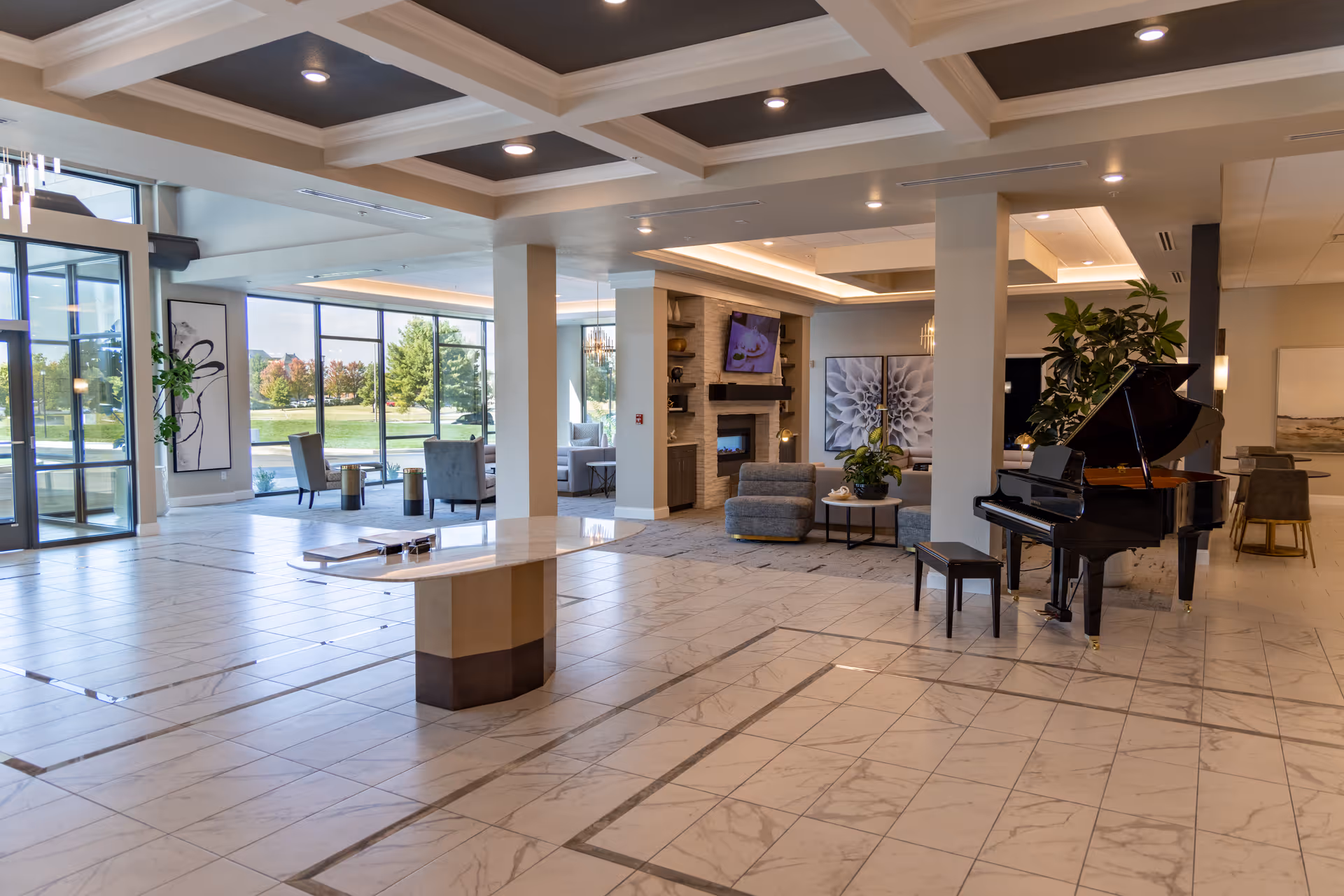 Spacious senior living facility lobby with marble floors, seating areas, a grand piano and large windows.
