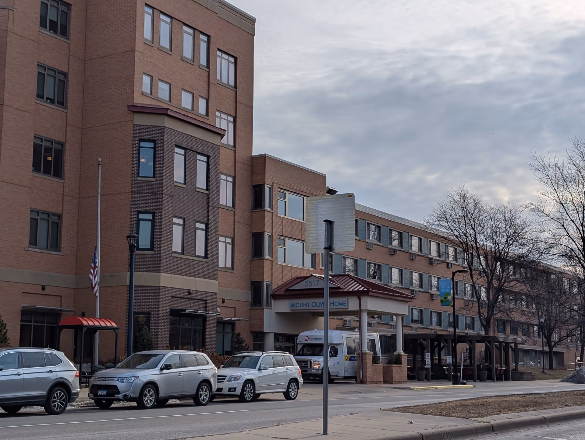 Front exterior of the Mount Olivet Careview Home building with a covered entrance, parked cars, and a cloudy sky.