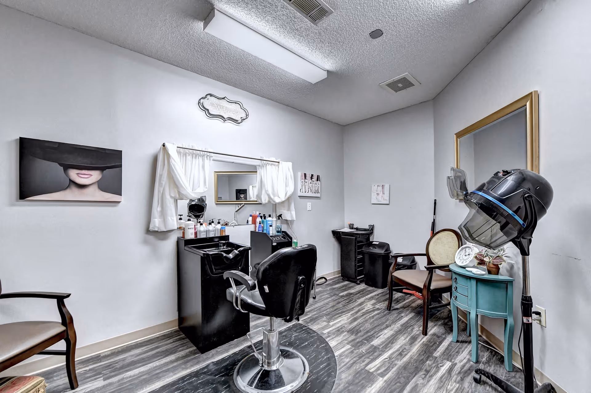 A small salon/styling room with a barber chair, shampoo sink, hooded hair dryer, mirrors and styling products.
