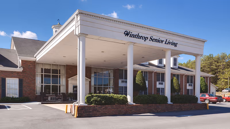 Front entrance of a brick senior living facility with a covered portico reading 'Winthrop Senior Living'.
