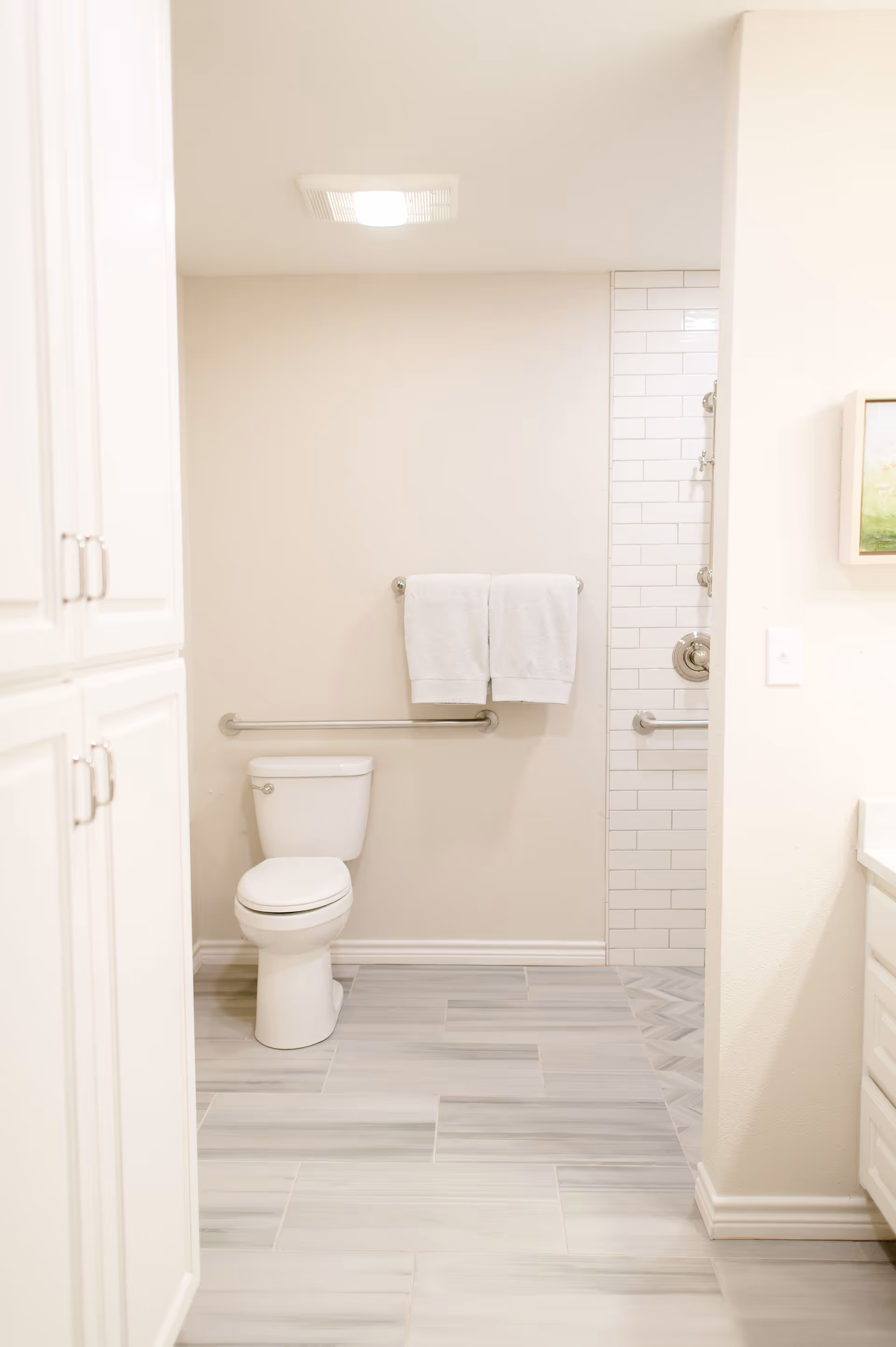 Bright accessible bathroom with a toilet, grab bars, a towel on a rack, and a tiled shower area.