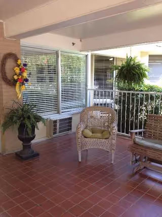 Covered outdoor patio with wicker chairs, potted plants, windows, and a railing.
