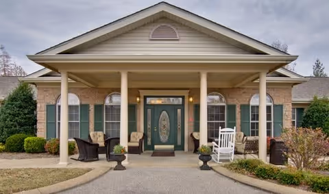 Covered front entrance of Alexandria Place with columns, seating, planters and double glass doors.