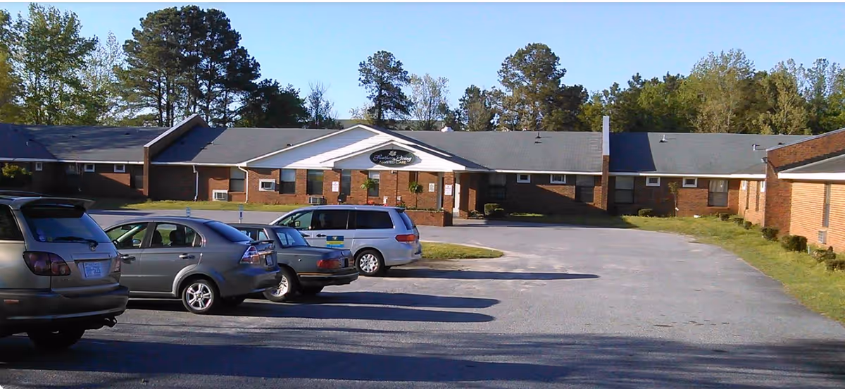 Front view of a single-story brick senior living building with a covered entrance and several cars parked in the lot.