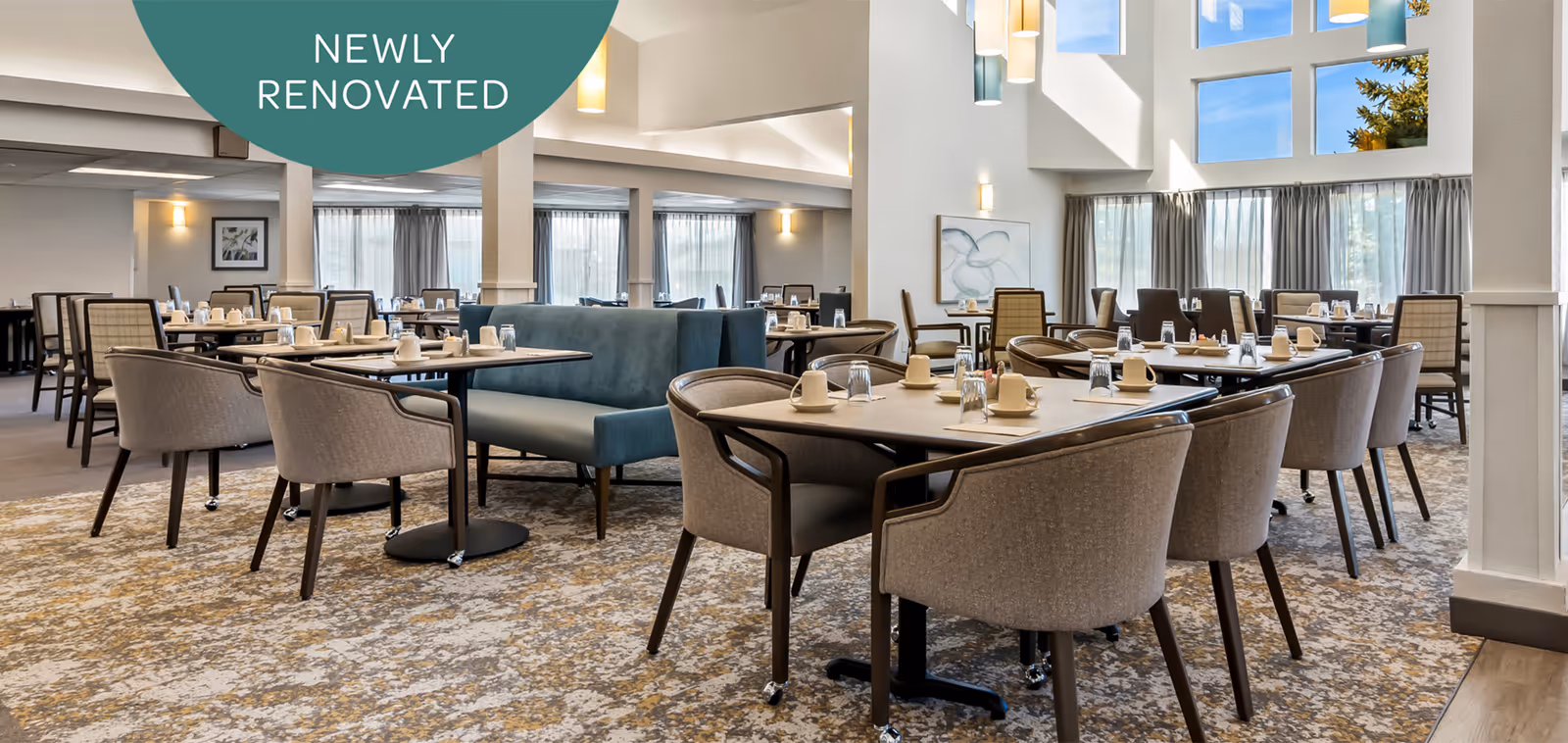 A newly renovated dining room with multiple tables and chairs arranged neatly. Each table is set with cups, glasses, and napkins. The room features large windows with curtains allowing natural light to fill the space, and there is a high ceiling with modern light fixtures.