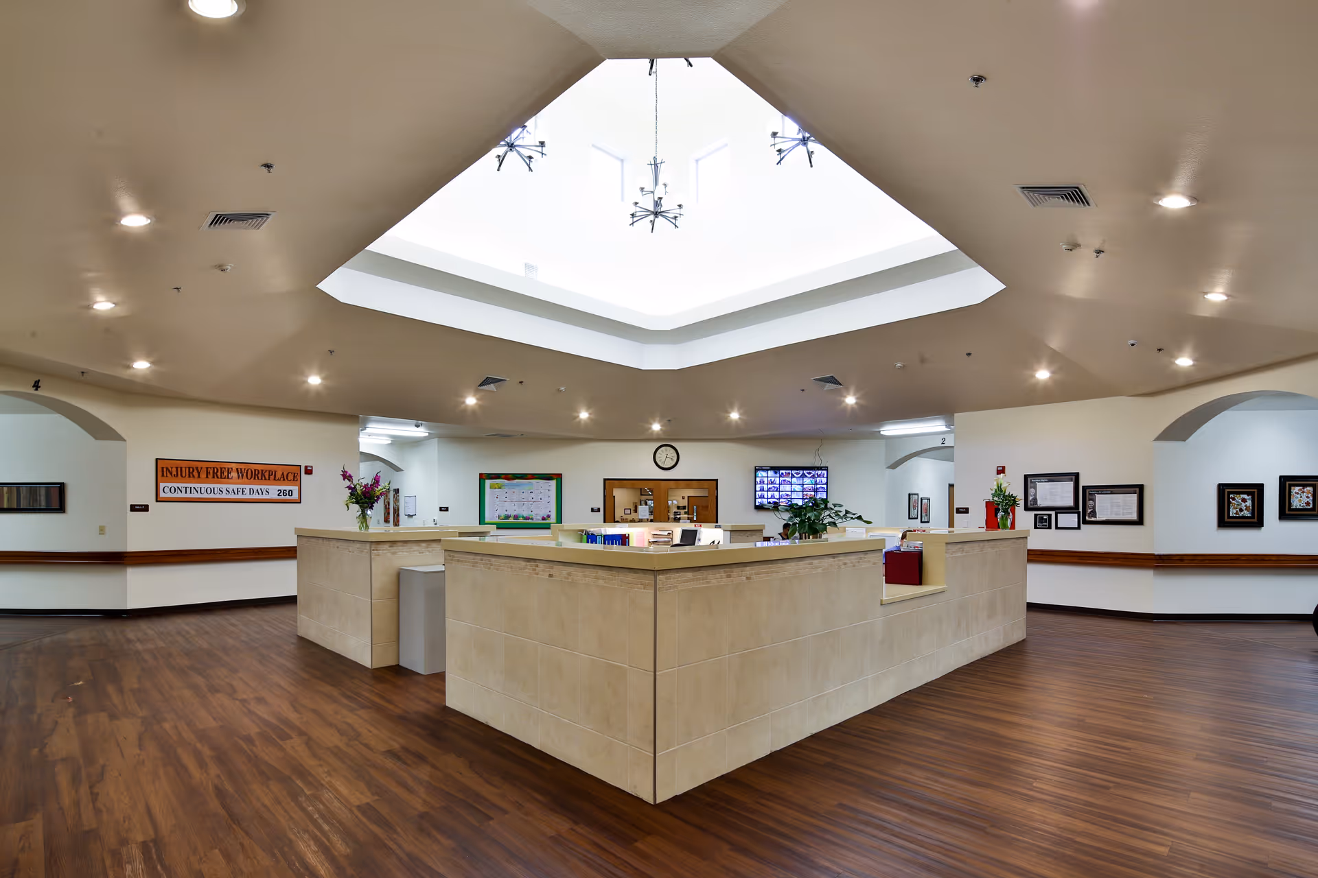 Spacious reception desk area inside a senior living facility with a central skylight and wood floors.