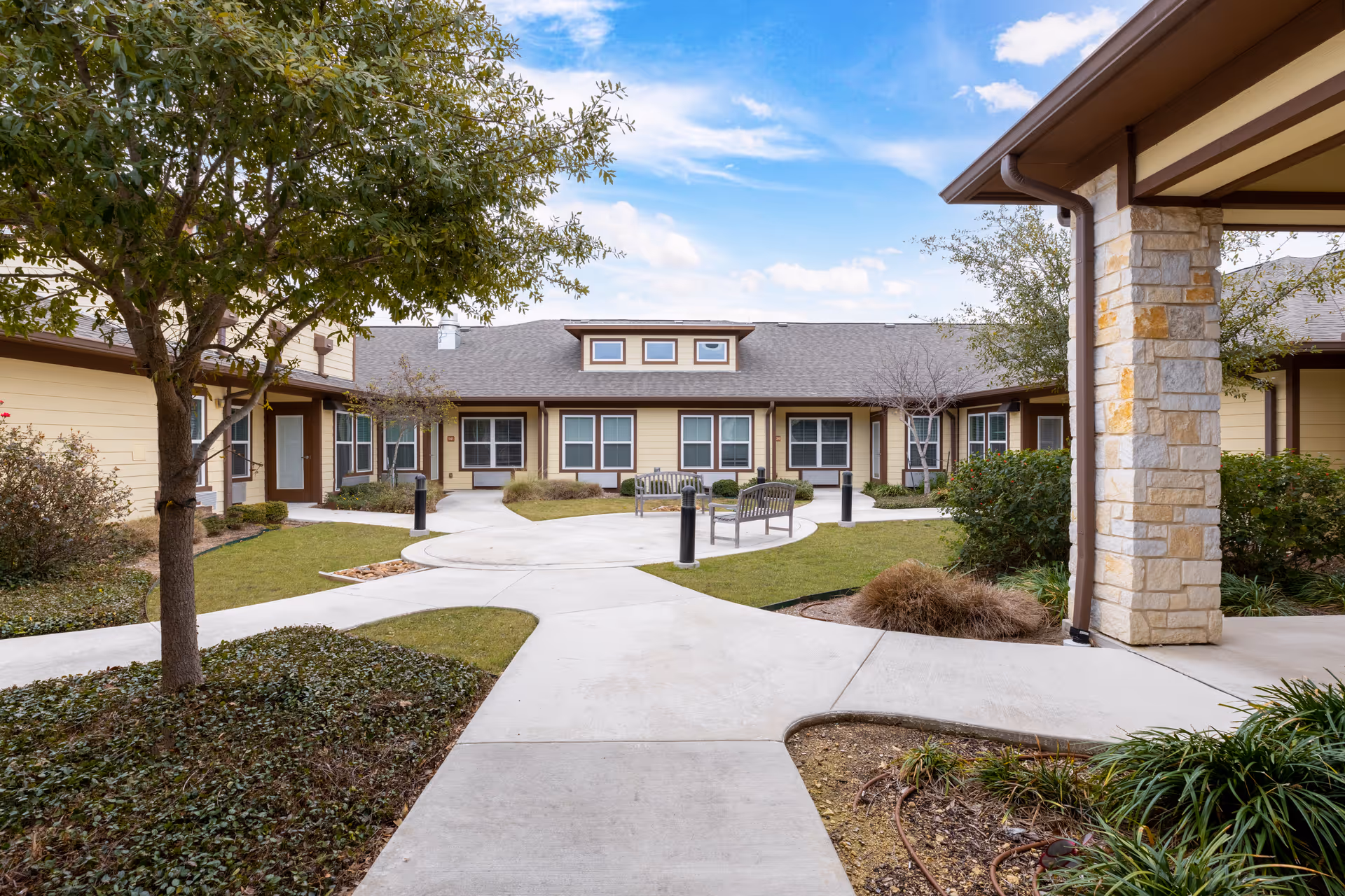 Courtyard with walkways, benches, and landscaping surrounded by single-story senior living residences.