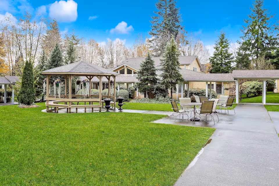 Green courtyard featuring a wooden gazebo and outdoor seating in front of cottage-style buildings.