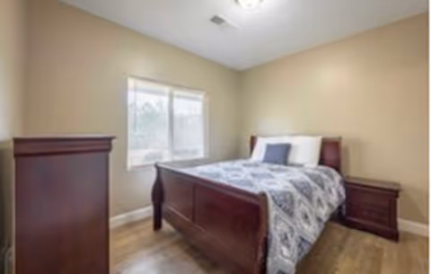 Sunlit bedroom with a wooden bed, matching dresser and nightstand, and a window.