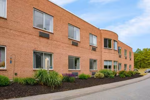 Brick senior living facility exterior with manicured landscaping along a curved driveway.
