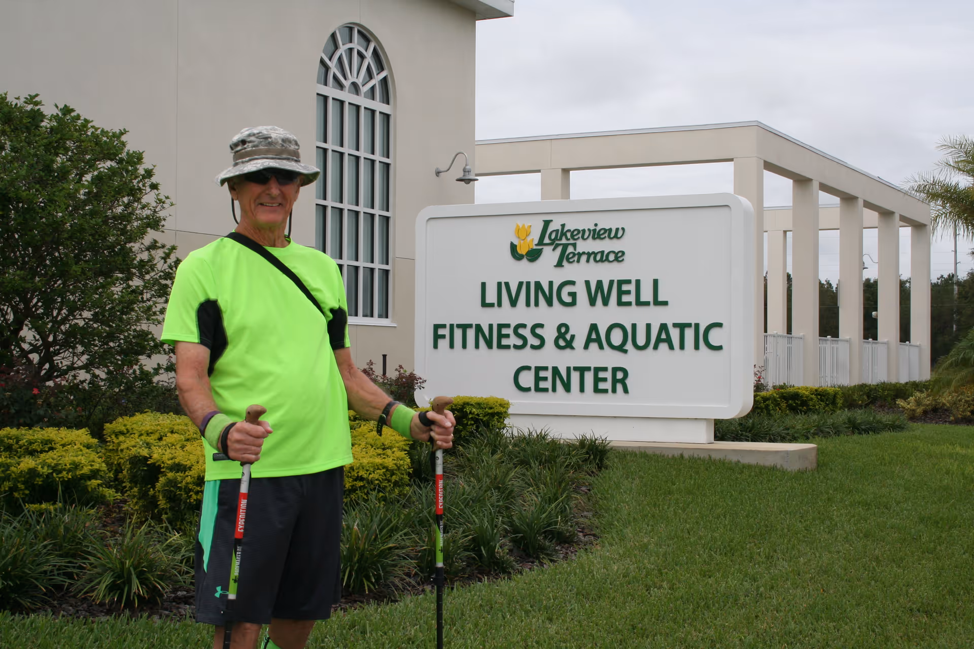 Man in neon shirt stands outside Lakeview Terrace fitness sign near building.