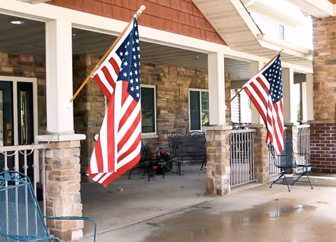 A stone and wood front porch of Copper Creek Senior Living with two American flags.