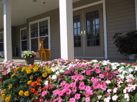 Colorful flowers line a front porch with columns and double doors.