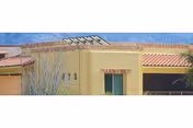 Partial exterior of a stucco building with a red tile roof, a small balcony, desert plants, and mountains in the background.
