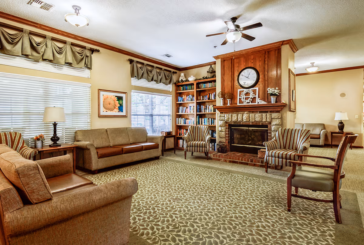Cozy senior living lounge with sofas, chairs, fireplace, and bookshelves.