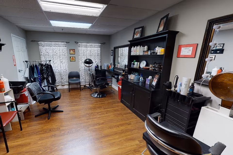 Interior salon area with styling chairs, mirrors, shelving of hair products and a hooded dryer on a wood floor.
