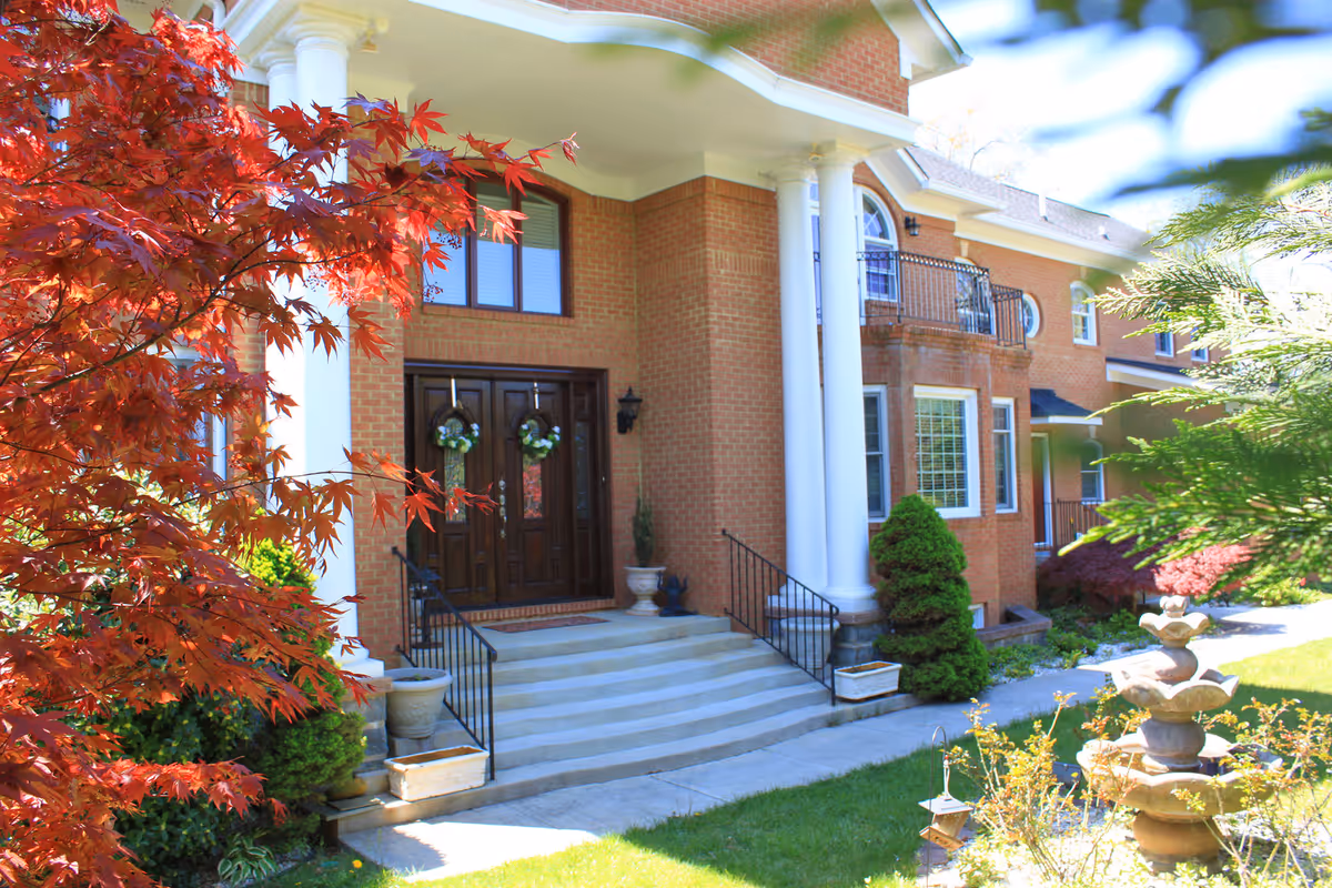 Brick senior living facility entrance features columns, stairs, a fountain, and a landscaped front yard.