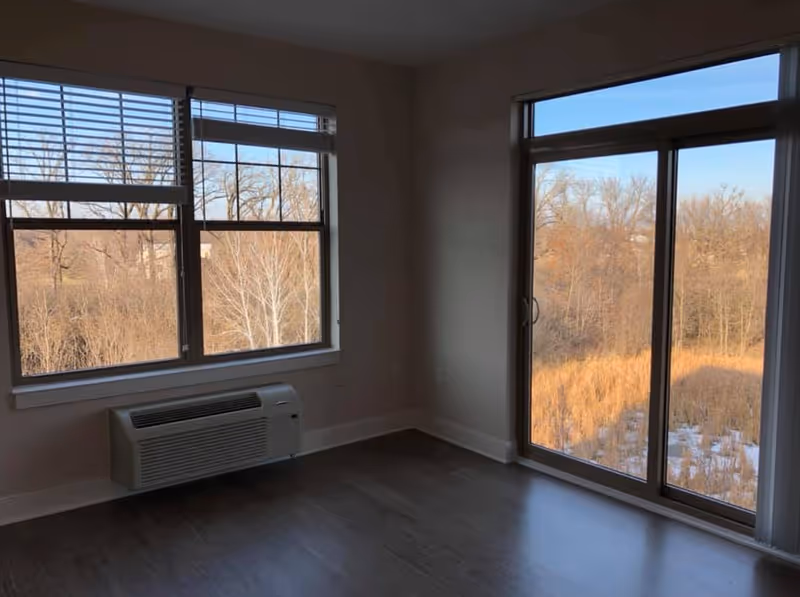 Empty room with large windows and a sliding glass door overlooking a wooded area.