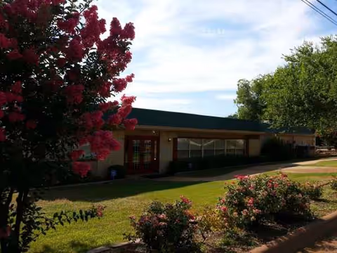 A single story assisted living building with a landscaped lawn and flowering trees in front.