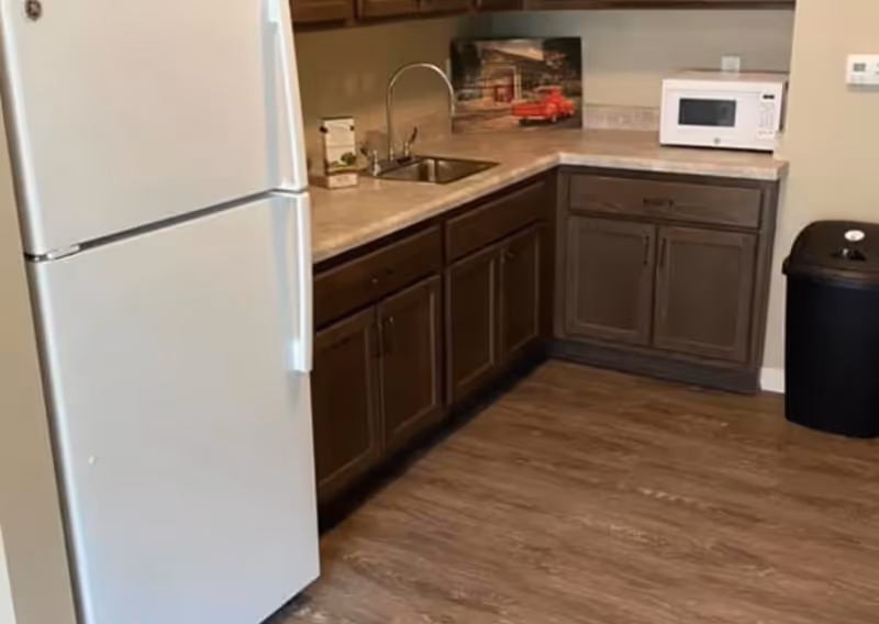 Small kitchenette with a white refrigerator, dark wood cabinets, a sink and microwave on a laminate countertop.
