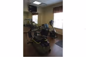 Small exercise room with two recumbent stationary bikes, an upright bike, a wall-mounted TV, and windows.