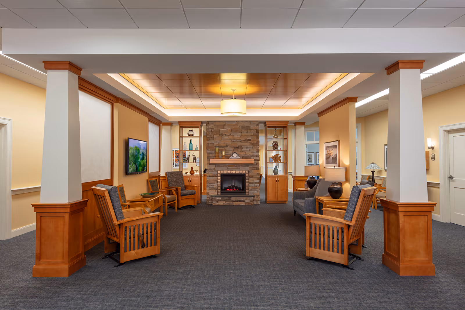 Spacious communal lounge with wooden chairs and sofas facing a stone fireplace under a coffered ceiling.