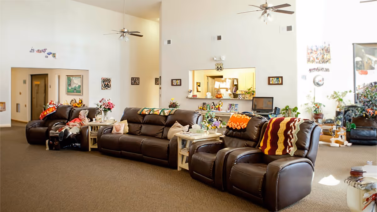 Spacious assisted-living common room with several leather recliner sofas, side tables, plants and decorative throws under high ceilings.